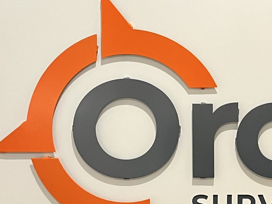 Close-up of layered orange and gray dimensional logo pieces on a white metal panel