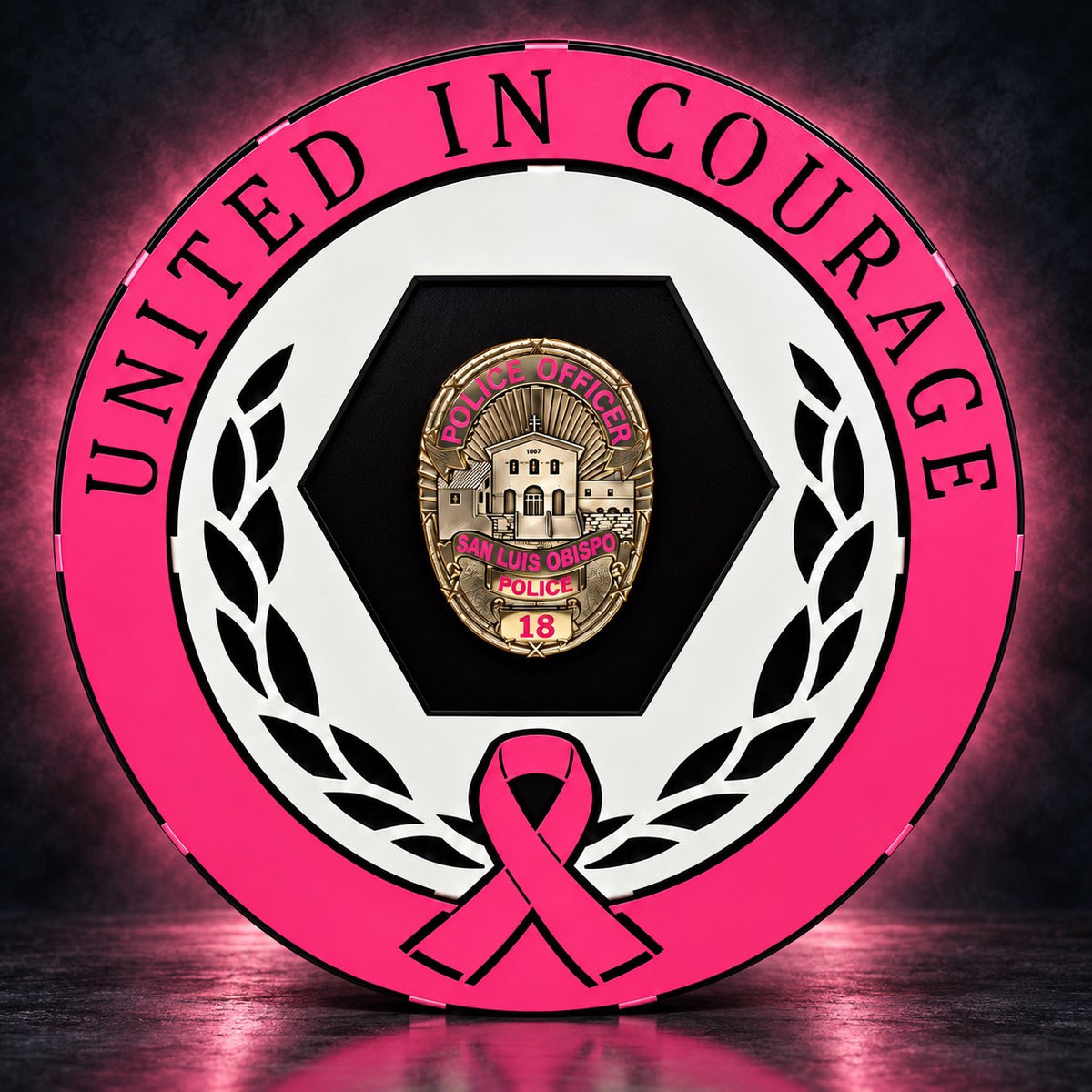 Breast Cancer Awareness badge display with a pink United in Courage band, white laurel and pink ribbon around a San Luis Obispo Police badge on a black hexagon panel, glowing pink on a dark background