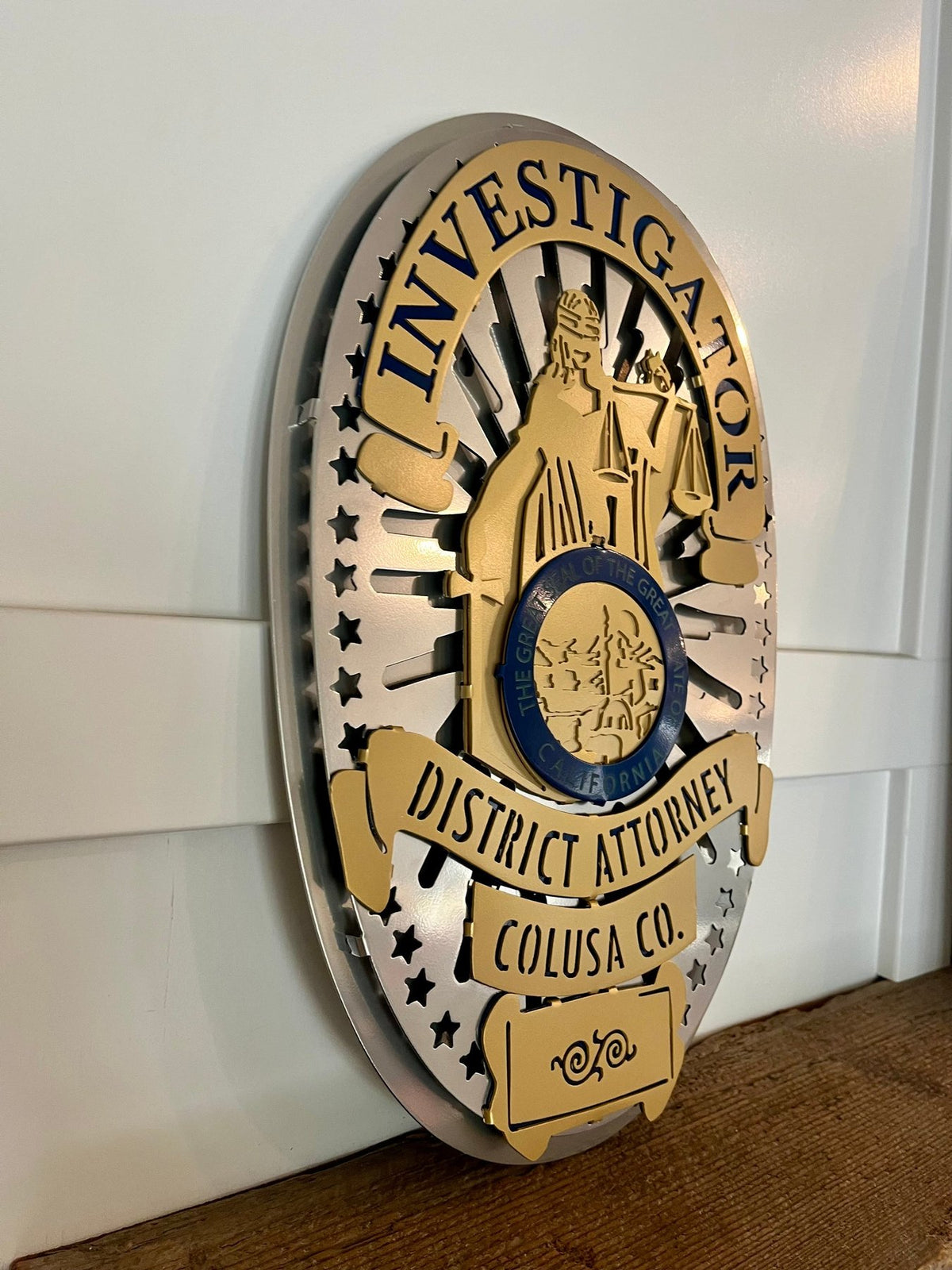 Gold and silver investigator badge on a wooden shelf, Colusa County DA Investigations by IRONiNK.