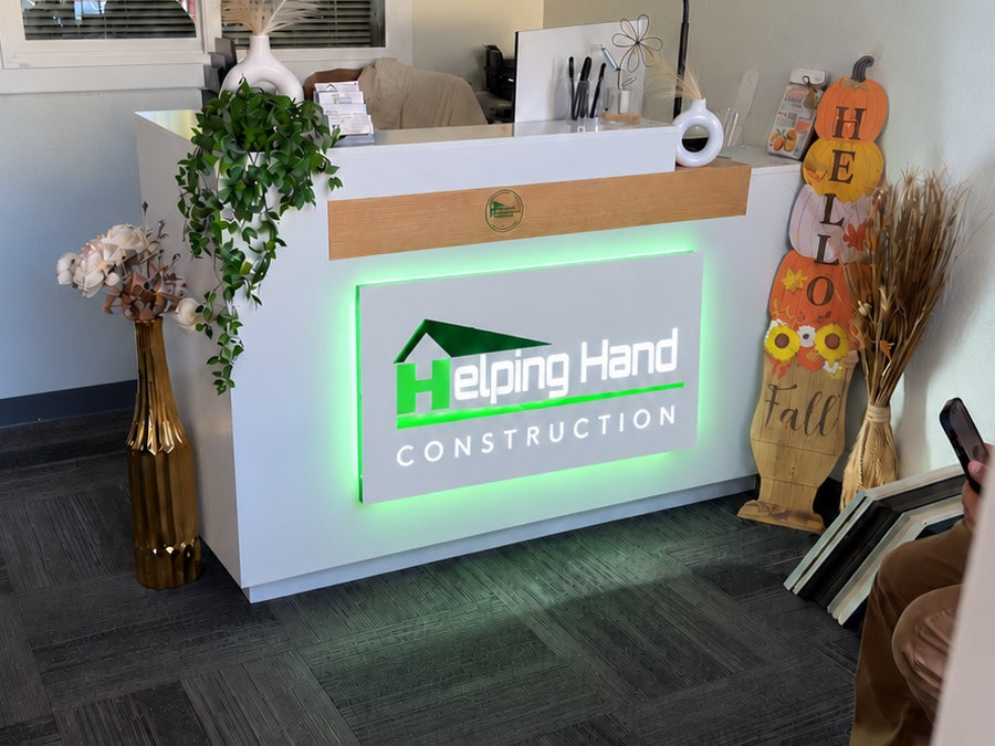 Helping Hand Construction reception desk sign with green LED backlighting glowing around the logo panel