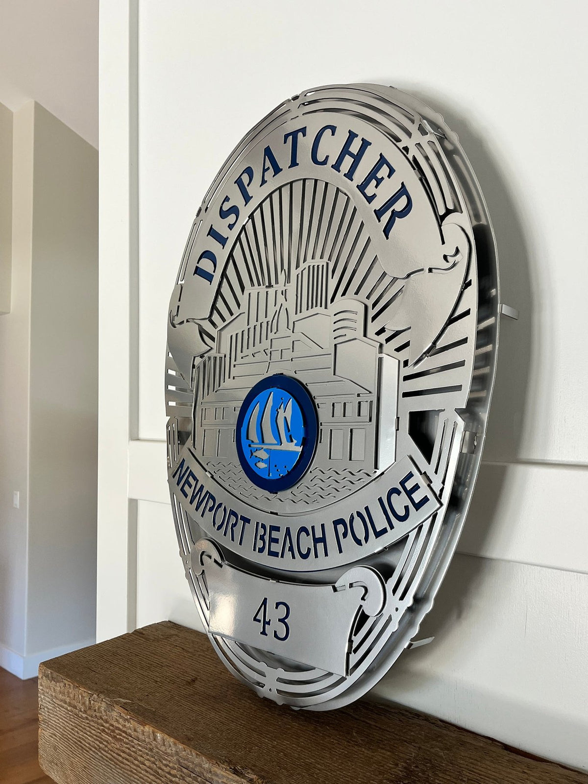 Silver dispatcher badge on a wooden shelf, Newport Beach Police Department Badge by IRONiNK.