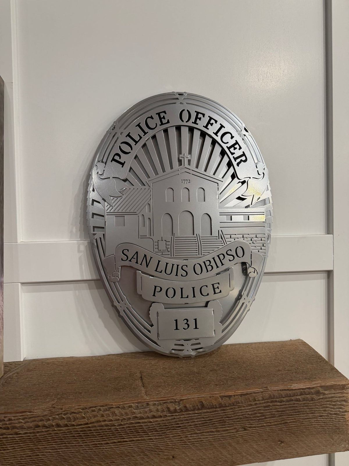 Silver badge displayed on a wooden shelf, San Luis Obispo Police Department by IRONiNK.