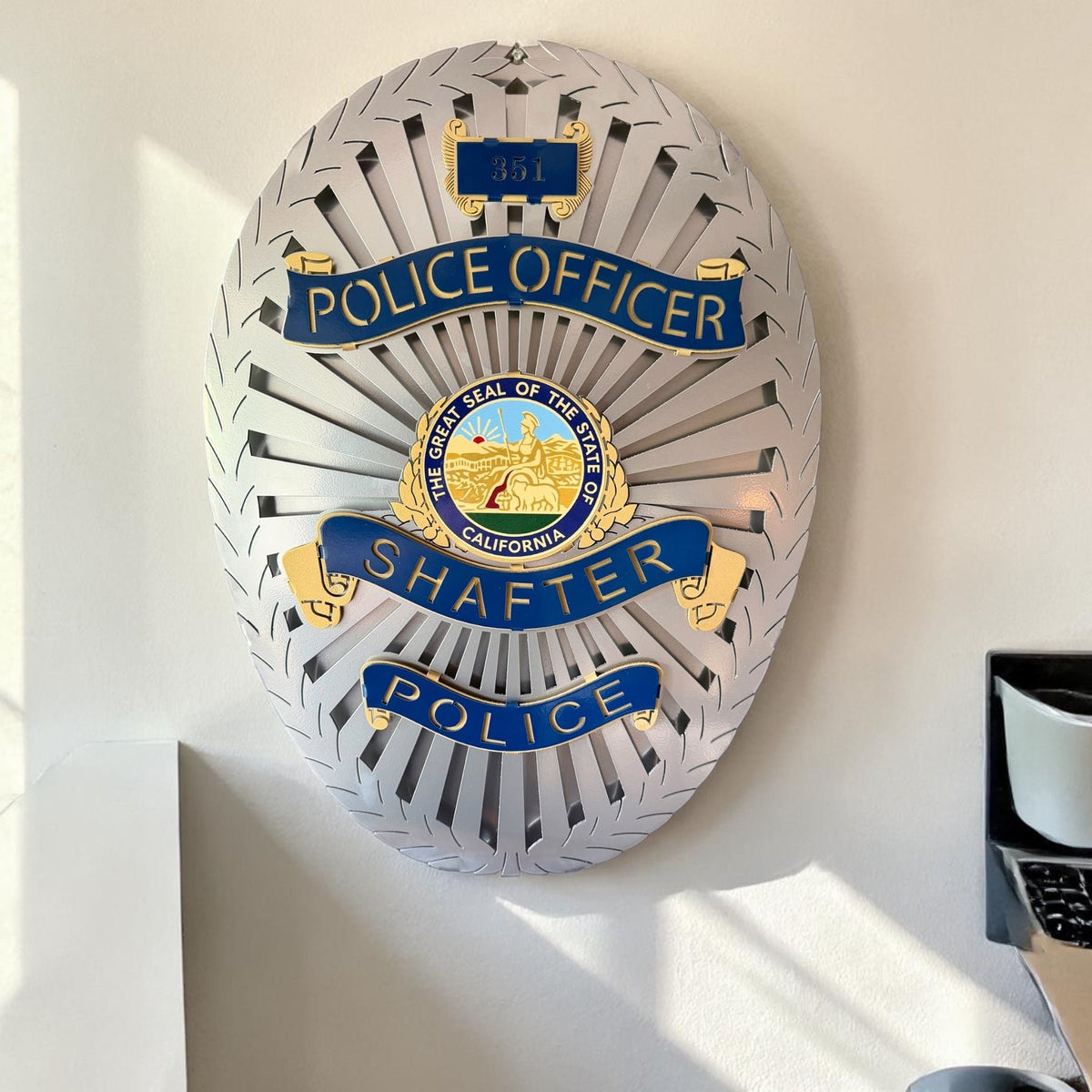 Silver and blue badge displayed beside a window, Shafter Police Department by IRONiNK.